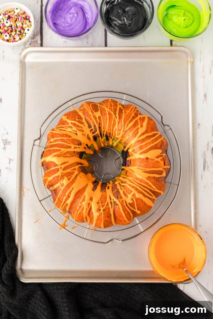 Bewitched Bundt Cake 21 Halloween Bundt Cake drizzled with orange frosting on a wire rack, with other colors of frosting ready nearby.