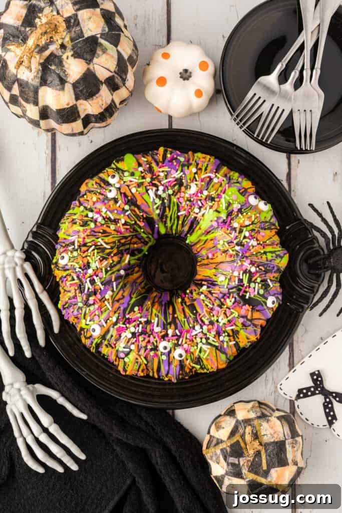 Bewitched Bundt Cake 24 Decorated Halloween Bundt Cake on a black platter surrounded by pumpkins, forks, and skeleton hand props