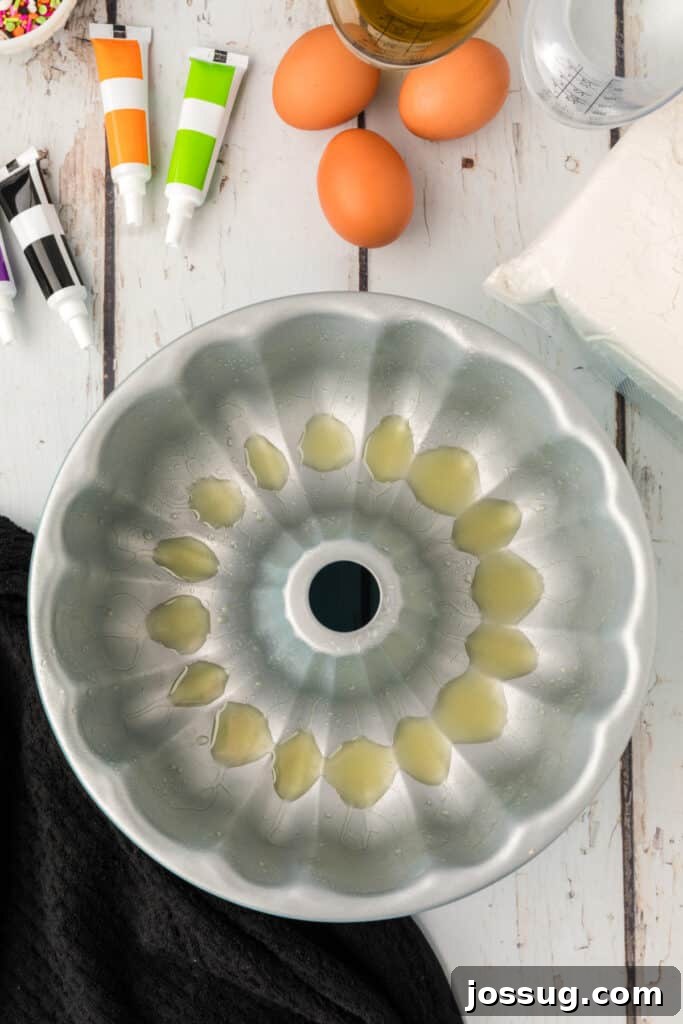 Bewitched Bundt Cake 4 Greased bundt pan surrounded by Halloween Bundt Cake ingredients like eggs, oil, flour mix, and colorful food coloring tubes.