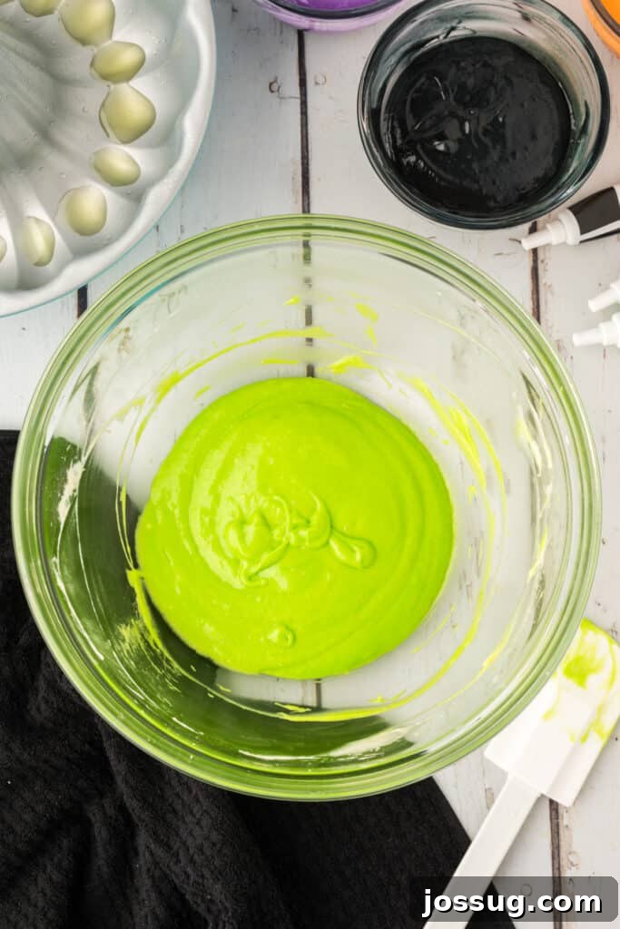 Bewitched Bundt Cake 10 Bowl of neon green cake batter with a spatula beside it, ready for layering in the bundt pan.