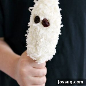 A delightful Boo-nana, a banana ghost treat, adorned with raisin eyes and coconut flakes, ready to be enjoyed for Halloween.