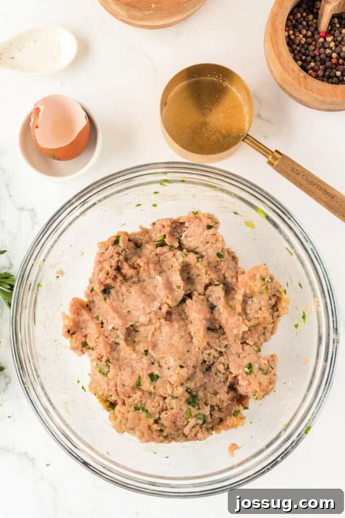 Ground chicken meatball mixture fully combined and evenly mixed in a clear glass mixing bowl on a white marble surface, showing proper consistency