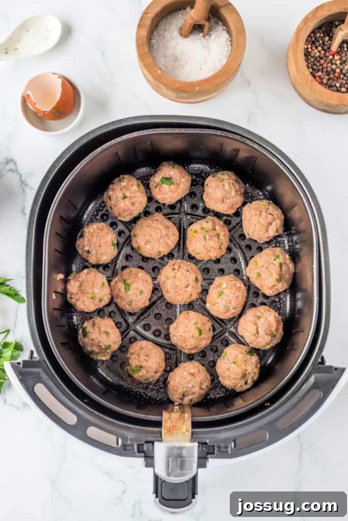 Uncooked chicken meatballs carefully arranged in a single layer inside the basket of an air fryer, ensuring space between each for optimal hot air circulation before cooking