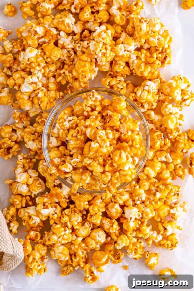 Overhead view of a clear bowl filled with glistening golden caramel corn, with loose caramel popcorn kernels scattered around on a sheet of parchment paper, highlighting its inviting texture.