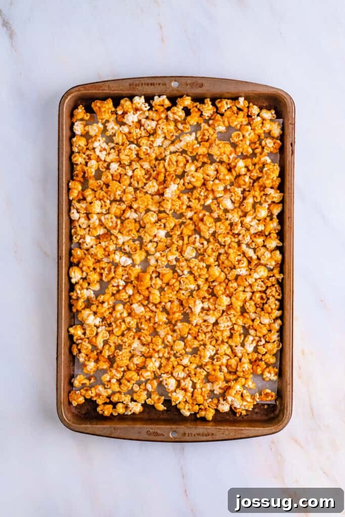 Finished caramel corn beautifully spread out on a baking sheet lined with parchment paper, golden and glistening after baking, cooling to perfection and ready to be broken apart into irresistible clusters.