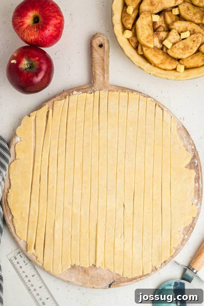 Precisely cut strips of pie dough neatly laid out on a wooden board, organized and ready to be woven into an intricate lattice pattern for the apple pie's top.