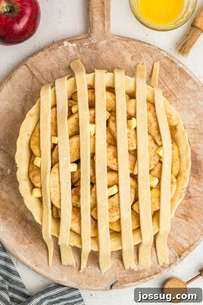A partially assembled apple pie, with the initial vertical lattice strips carefully placed over the spiced apple filling, demonstrating the weaving process.