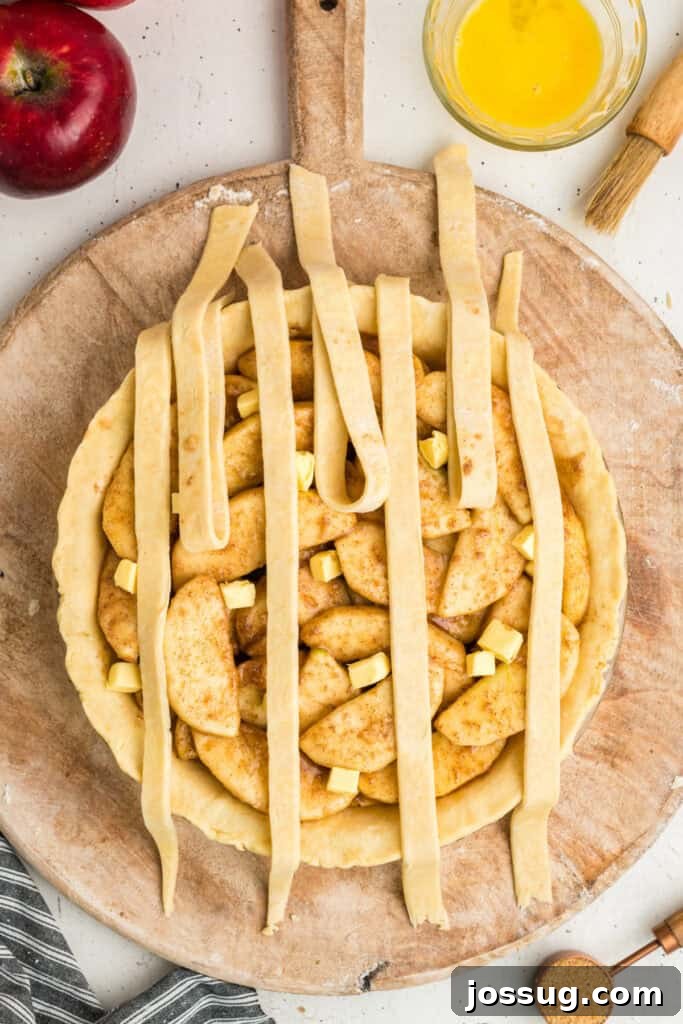 An apple pie in progress, with delicate lattice strips being woven into a beautiful pattern, with an egg wash and coarse sugar waiting nearby for the finishing touches.