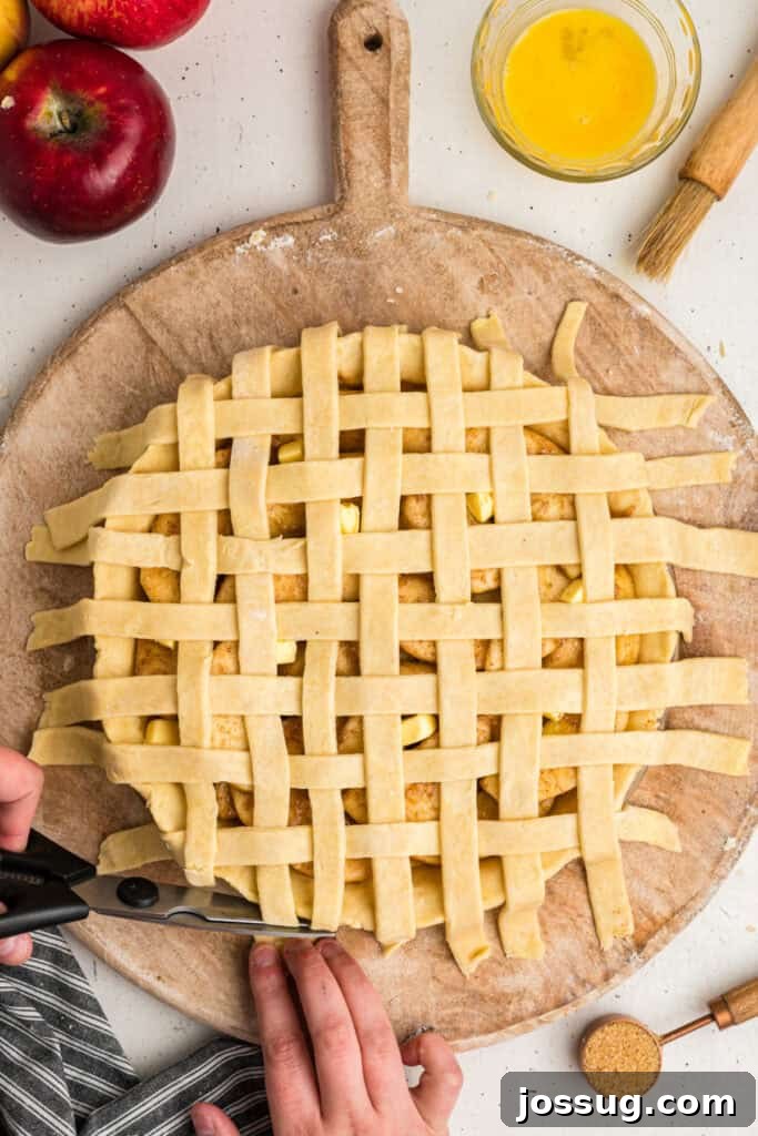 Kitchen scissors expertly trimming excess lattice dough from the edges of the apple pie, ensuring a neat and professional finish to the crust.