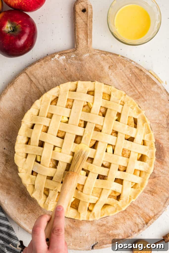 A pastry brush meticulously applying a glistening egg wash over the intricate lattice crust of an unbaked apple pie, preparing it for a golden-brown finish.
