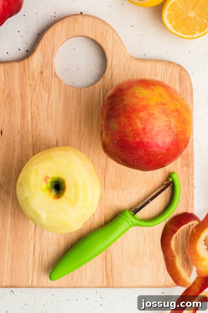 Fresh apple being peeled with a green peeler on a wooden cutting board, highlighting the crispness of the fruit.