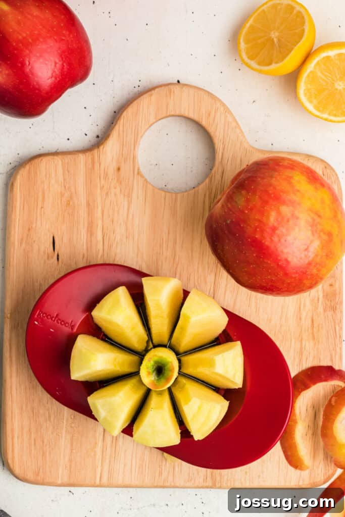 An apple precisely sliced into uniform wedges with a red apple corer on a rustic wooden cutting board.