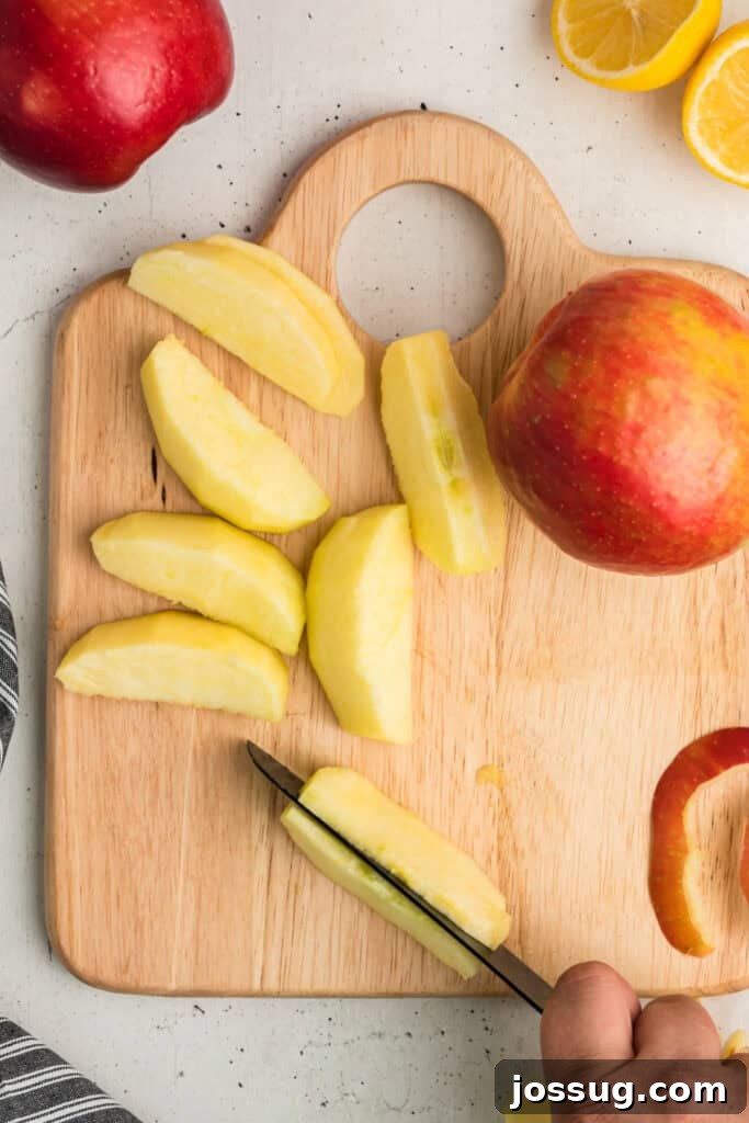 Apple wedges being carefully cut into thinner, consistent slices with a sharp knife on a cutting board, ready for the filling.