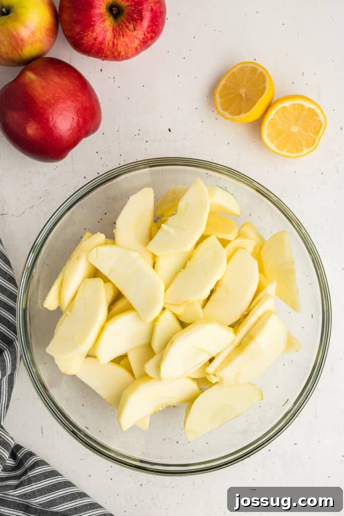 A bowl brimming with freshly sliced apples, with a halved lemon and whole apples artfully arranged nearby, showcasing the fresh ingredients.