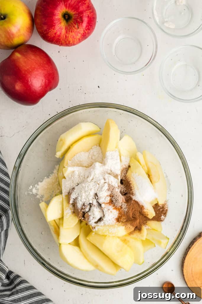 A mixing bowl filled with crisp sliced apples, generously topped with a blend of flour, granulated sugar, and aromatic spices, awaiting a good stir.