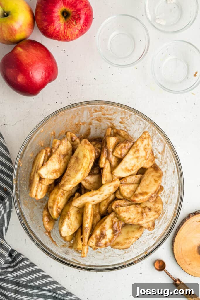 Perfectly sliced apples, glistening with a coating of sugars and fragrant spices, after being thoroughly mixed in a clear glass bowl, ready for the pie.