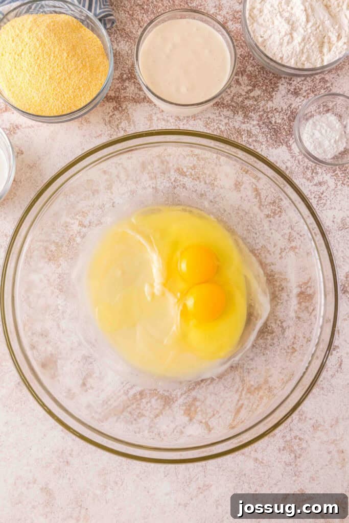 Cultured Cornbread 6 Two eggs cracked into a bowl with melted butter and sugar mixture, surrounded by bowls of ingredients.