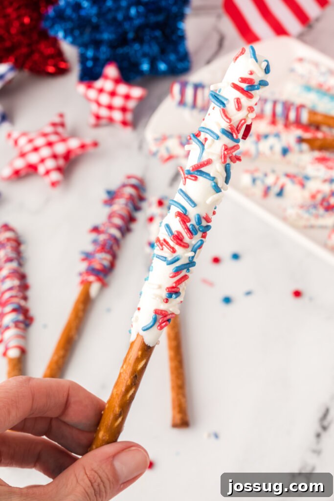 A hand holding a beautifully decorated chocolate dipped pretzel rod, ready to enjoy.