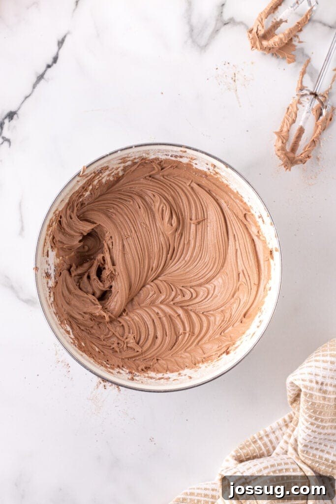 Bowl of freshly whipped Nutella buttercream frosting, showcasing its creamy and fluffy texture, with beaters nearby.