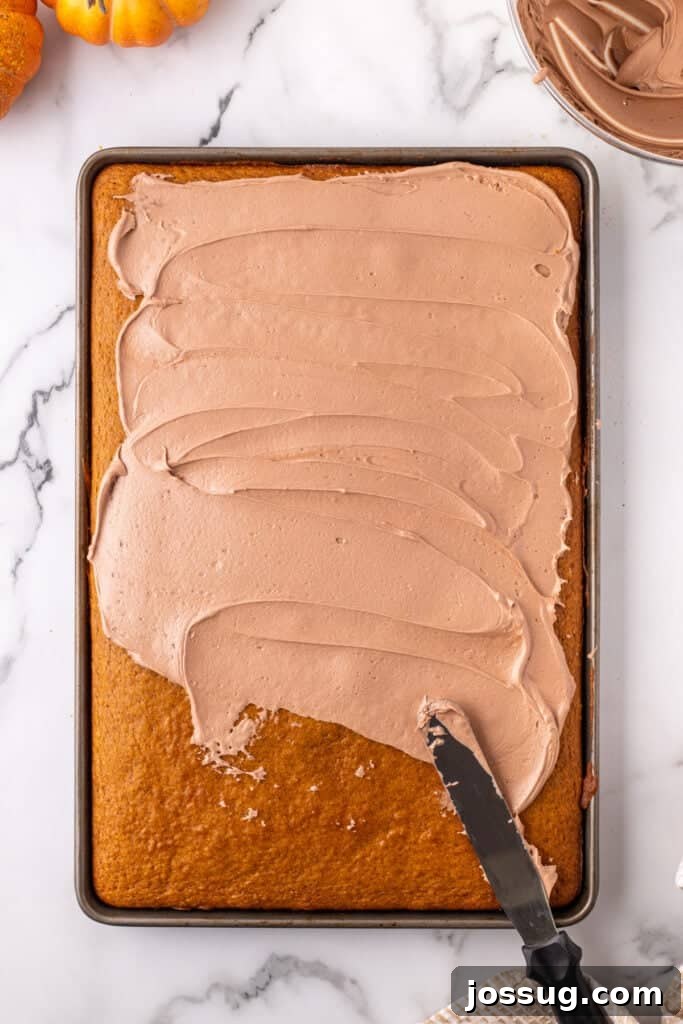 Pumpkin bars being frosted with smooth Nutella buttercream using an offset spatula on a baking sheet, ensuring even coverage.