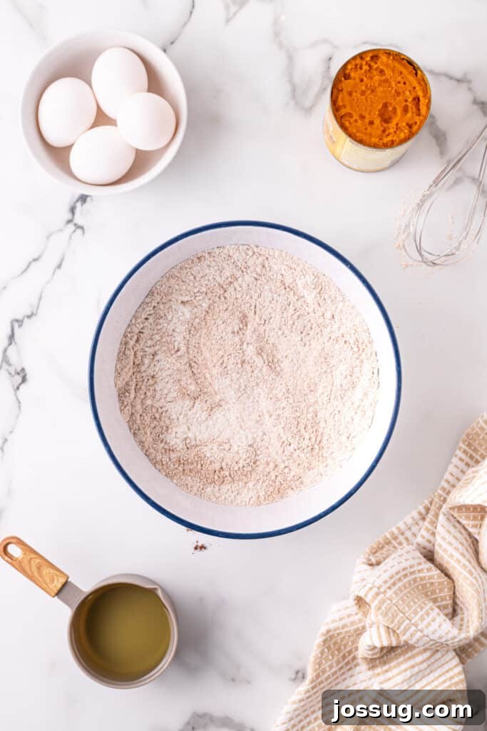 Dry ingredients for pumpkin bars, including flour, sugar, and spices, perfectly whisked together in a large white bowl on a marble surface.