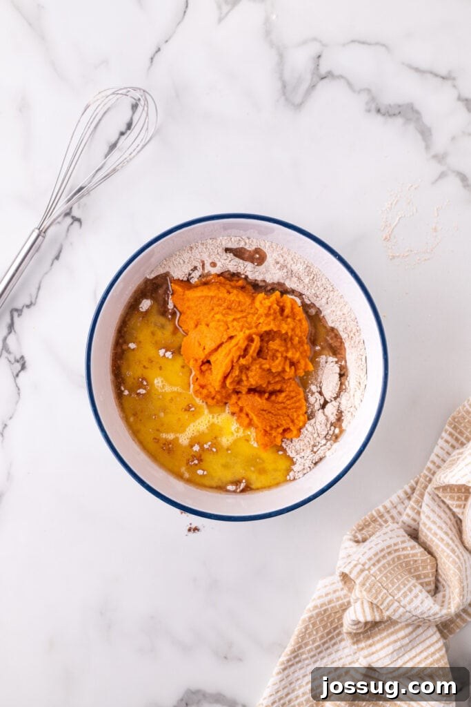 Pumpkin puree, beaten eggs, and vegetable oil added to the bowl of dry ingredients, ready for mixing to create the pumpkin bar batter.