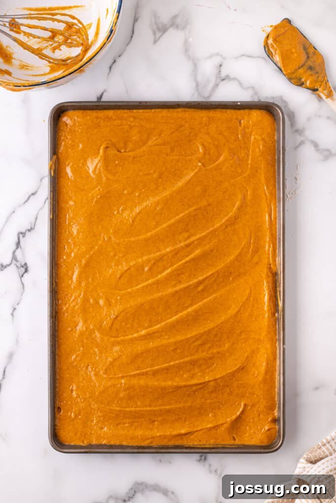 Pumpkin bar batter spread evenly into a parchment-lined baking sheet, ensuring a uniform thickness for baking.