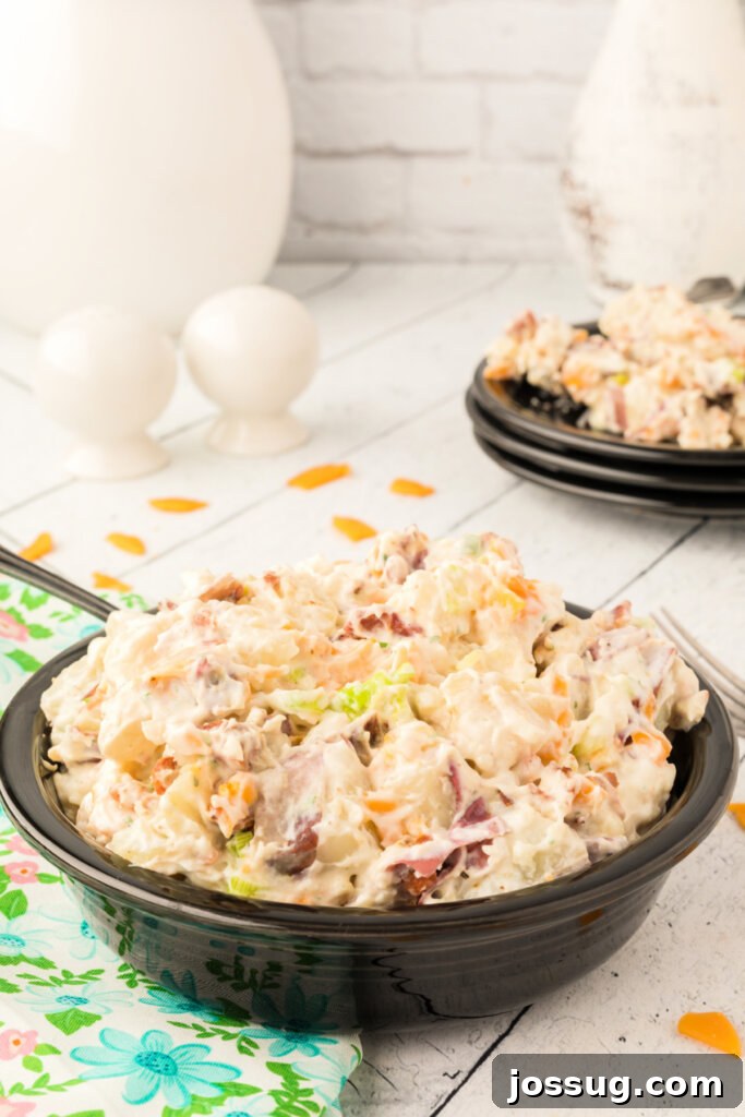 A large serving bowl filled with creamy Bacon Ranch Potato Salad, accompanied by a spoon, showcasing the delicious blend of potatoes, ranch dressing, bacon, and green onions.