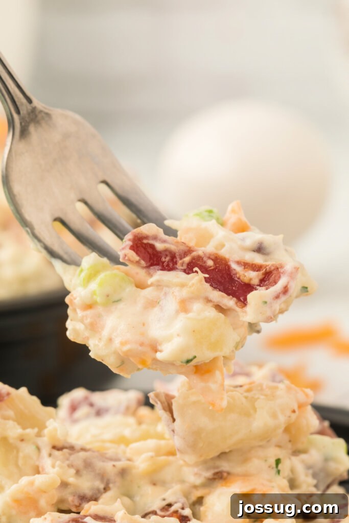 A fork holding a bite of Bacon Ranch Potato Salad, clearly showing the chunks of potato, bits of crispy bacon, and creamy dressing.