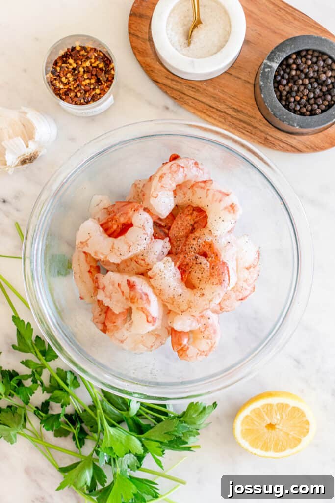 Succulent Air Fryer Garlic Butter Shrimp 4 A bowl of raw, pristine shrimp, meticulously seasoned with salt and black pepper, is elegantly presented on a marble surface. It is artfully surrounded by fresh parsley, vibrant lemon slices, and a selection of exotic spices, all meticulously arranged and ready for the culinary journey.