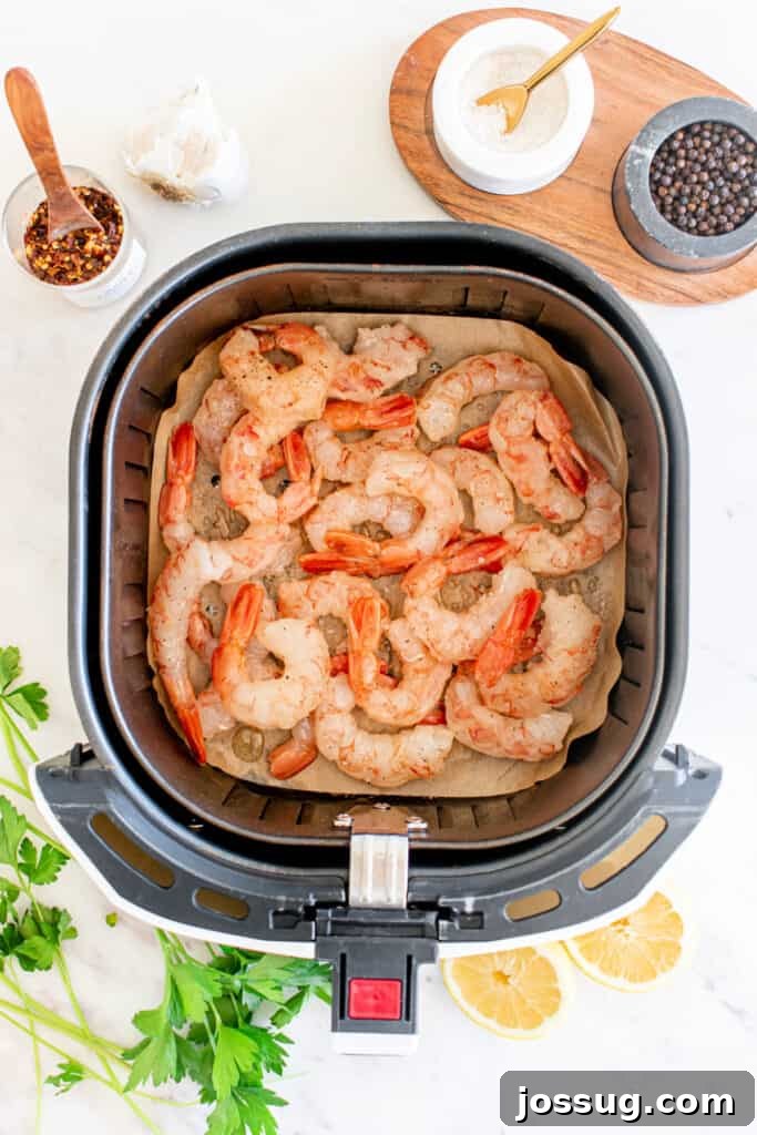 Succulent Air Fryer Garlic Butter Shrimp 5 Raw shrimp meticulously placed in a single, even layer inside an air fryer basket, thoughtfully lined with parchment paper to prevent sticking. Fresh garlic cloves and assorted spices are visible nearby, awaiting their turn to infuse flavor.