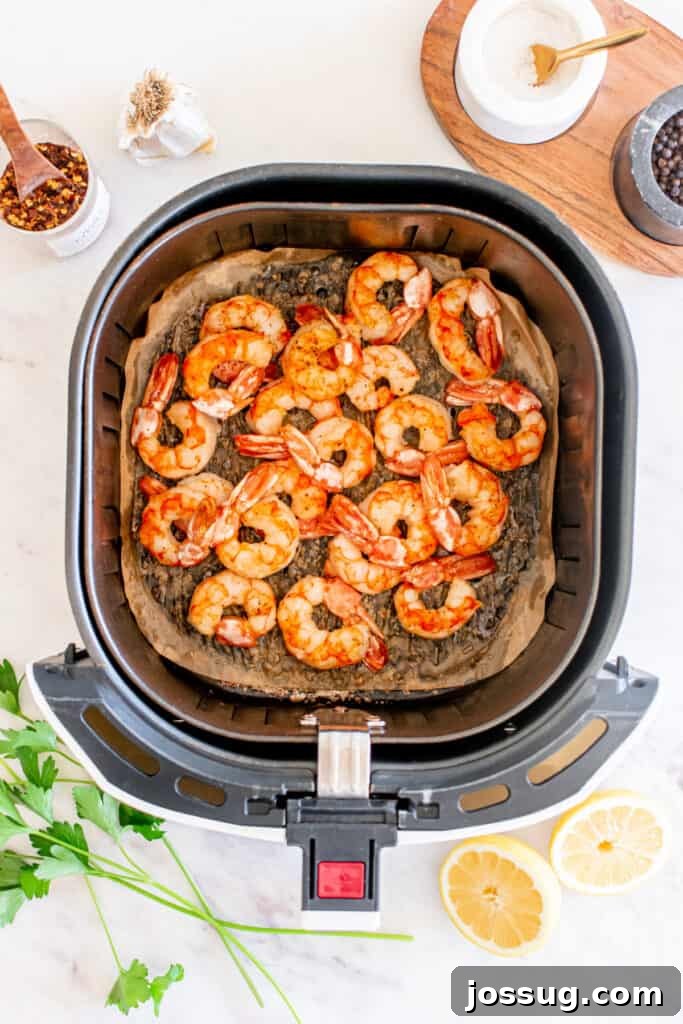 Succulent Air Fryer Garlic Butter Shrimp 6 Perfectly cooked shrimp resting in the air fryer basket, exhibiting a bright orange hue and a lightly crisp texture. The shrimp are artfully surrounded by vibrant lemon halves and fresh green parsley, creating an enticing and colorful display.