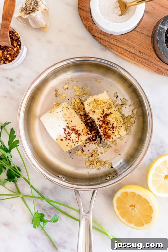 Succulent Air Fryer Garlic Butter Shrimp 7 A rich, golden mixture of creamy butter, finely minced garlic, fragrant black pepper, and vibrant red pepper flakes gently melting and simmering in a sleek stainless steel pan, beautifully set against a pristine marble countertop.