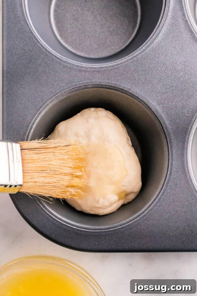 A basting brush applying melted butter onto the top of an apple pie bomb, preparing it for a luscious cinnamon-sugar coating.