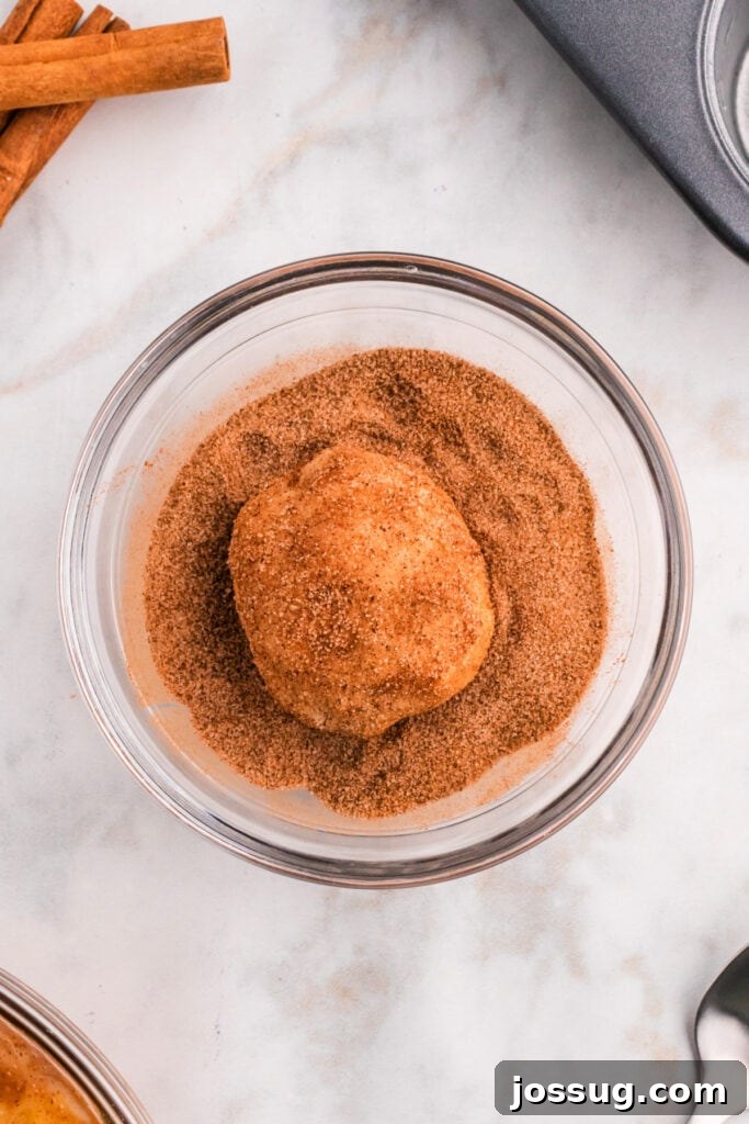 A golden biscuit dough ball, thoroughly coated in a delightful cinnamon-sugar mixture, poised to become a delicious apple pie bomb.