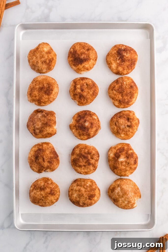 Freshly baked cinnamon sugar-coated apple pie bombs, glistening and golden brown, cooling on a baking sheet after emerging from the oven.