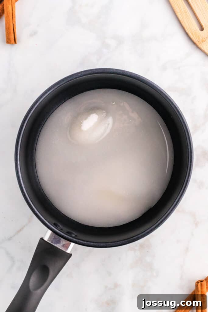 A saucepan on the stove, showing a sugar and water mixture beginning to dissolve, marking the first step in creating spiced caramel sauce.