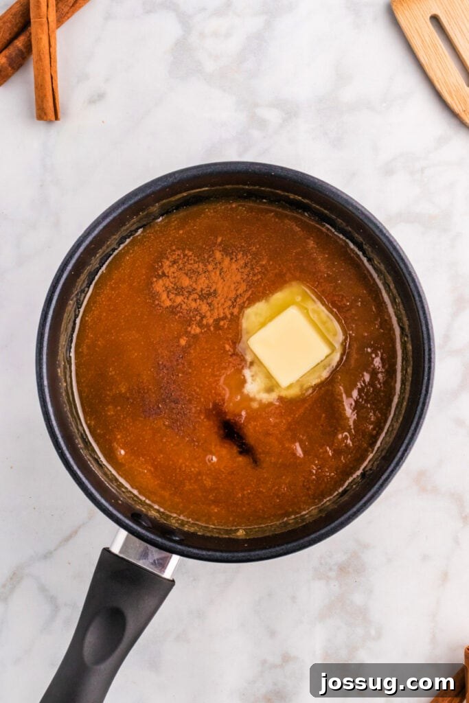 Butter, cinnamon, and vanilla extract being stirred into simmering spiced caramel sauce in a saucepan, infusing rich flavors.