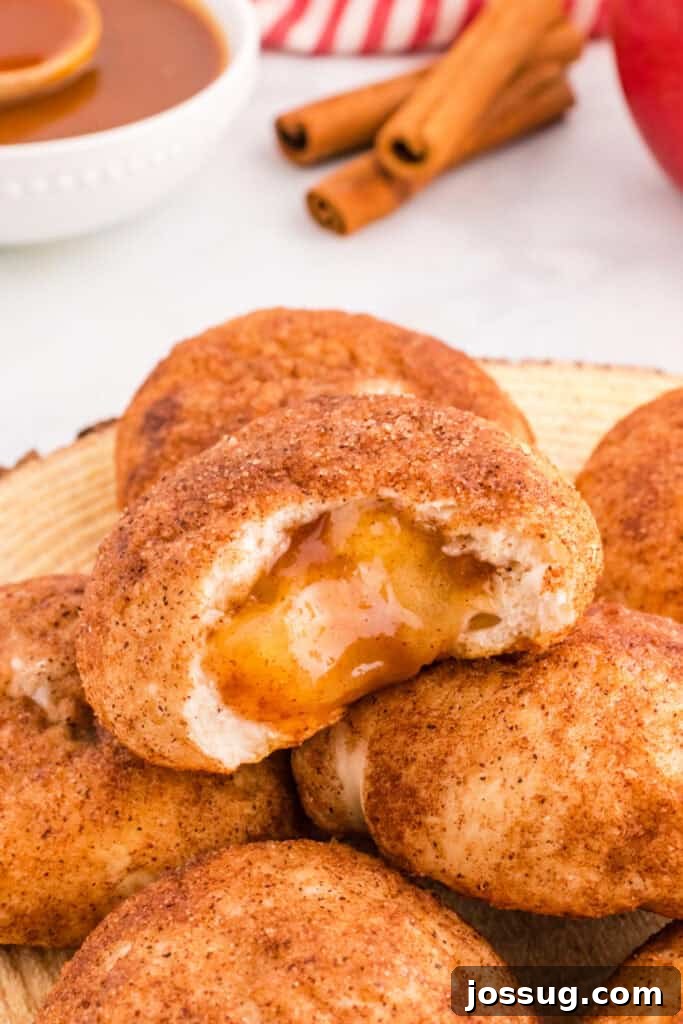 A close-up view of a baked apple pie bomb, cut open to reveal its irresistible gooey spiced apple filling spilling out.
