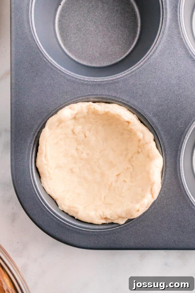 Biscuit dough pressed into a muffin pan cup, forming a perfect base for an apple pie bomb.