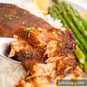 Close-up of flaky blackened salmon on a fork with rice and asparagus in the background.