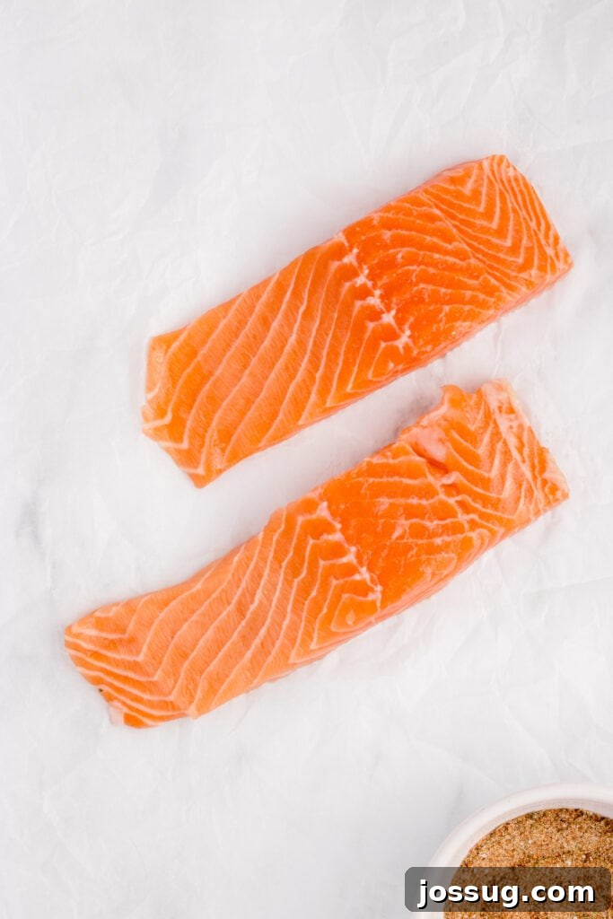 Two raw salmon fillets laid out on parchment paper next to a bowl of seasoning.