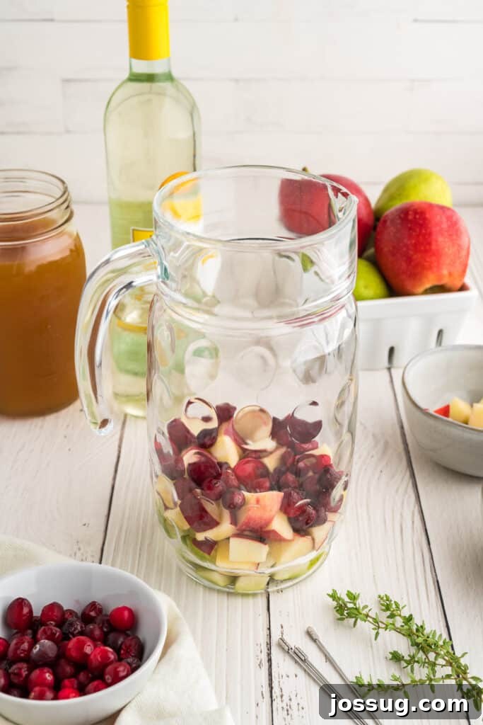 Autumn Orchard Sangria 4 Glass pitcher being filled with chopped apples, pears, and cranberries for apple cider sangria