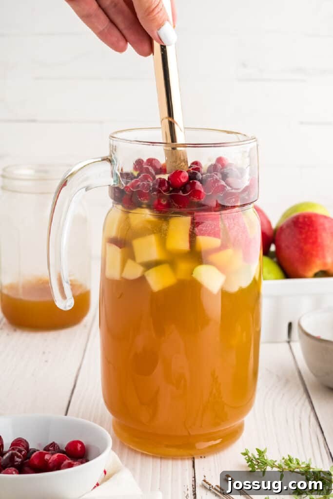 Autumn Orchard Sangria 6 Hand stirring a pitcher of apple cider sangria with fresh fruit and cranberries