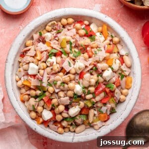 Overhead shot of grinder dense bean salad in a white serving bowl, garnished with fresh parsley.