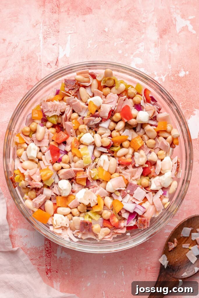 Grinding Bean Power Salad 4 Grinder dense bean salad partially mixed in a glass bowl showing beans, meats, cheese, and veggies.