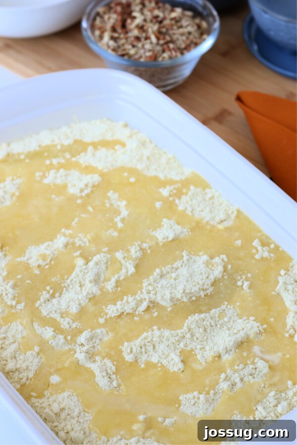 Spiced Pumpkin Crumble Bake 8 Melted butter being generously poured over the dry cake mix layer in the baking pan, creating a moist base for the final pecan topping.