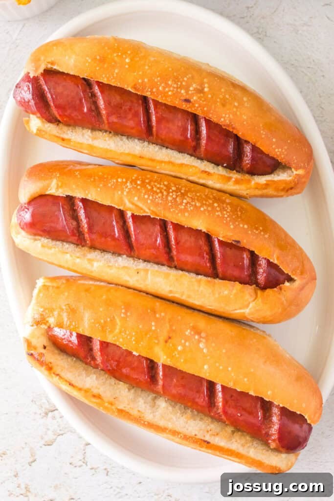 Three fully cooked hot dogs in toasted hoagie buns on a white platter