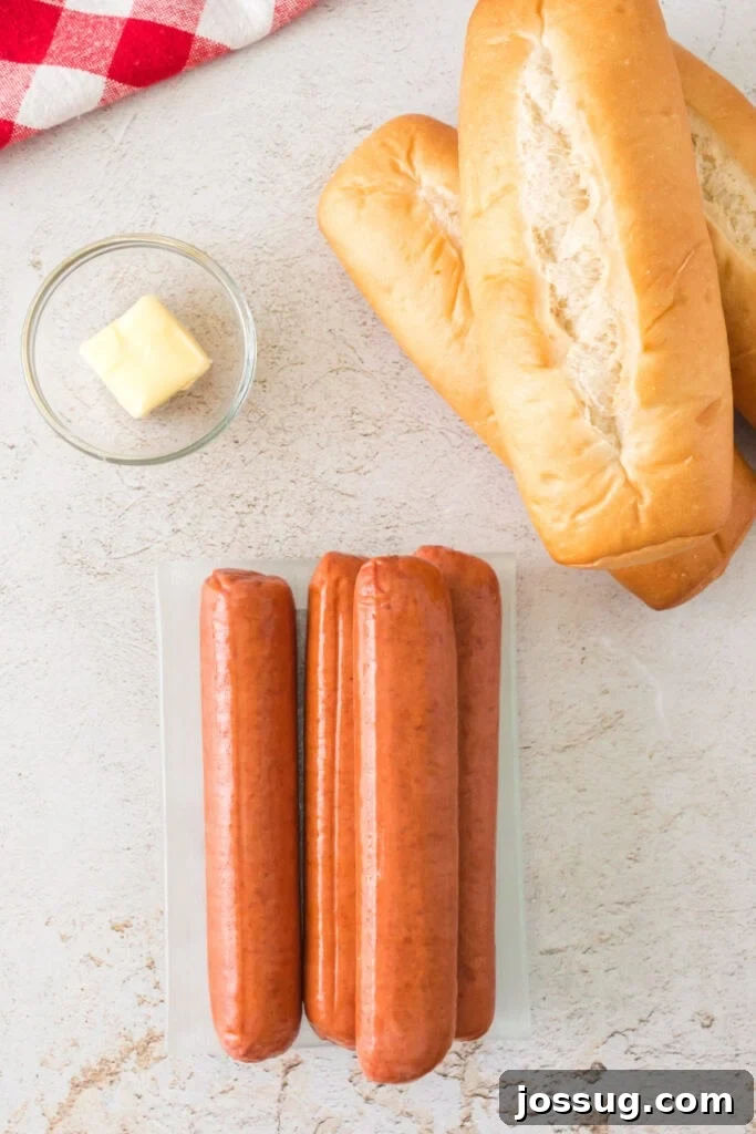 Raw hot dog sausages, hoagie buns, and a pat of butter on a light countertop