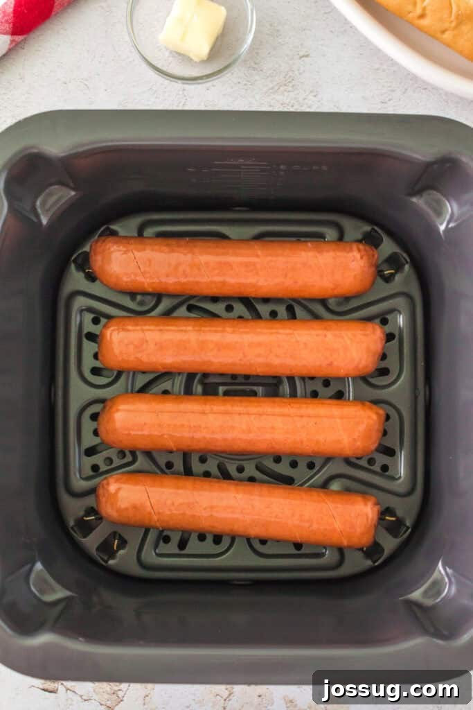 Four raw scored hot dog sausages placed in an air fryer basket